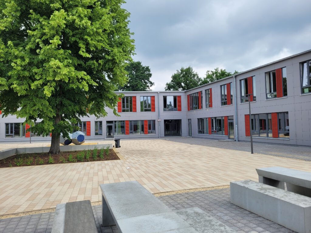 Außenansicht der Albert-Schweitzer-Schule mit Schulhof. Ein modernes, weißes, zweistöckiges Flachdach Gebäude